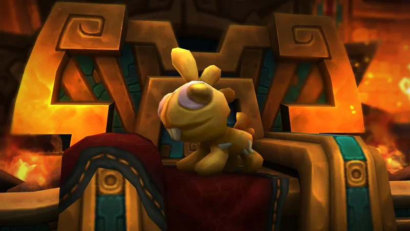 Ein goldgelbes Plüschtier in Gestalt eines kleinen Grrgle sitzt auf einem roten Polster vor einem Thron aus Stein und Gold